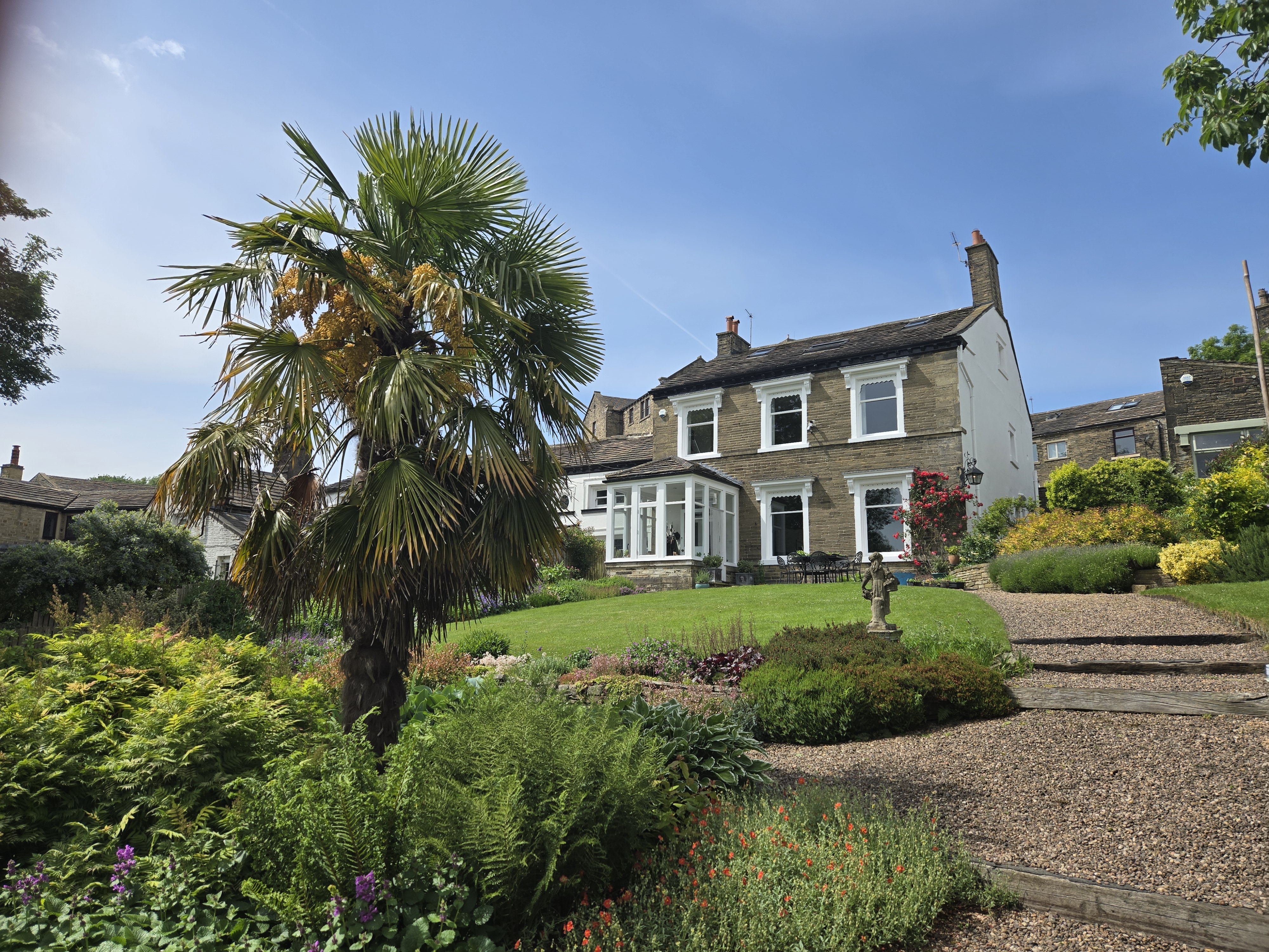 Stone built house with large garden and palm tree in foreground