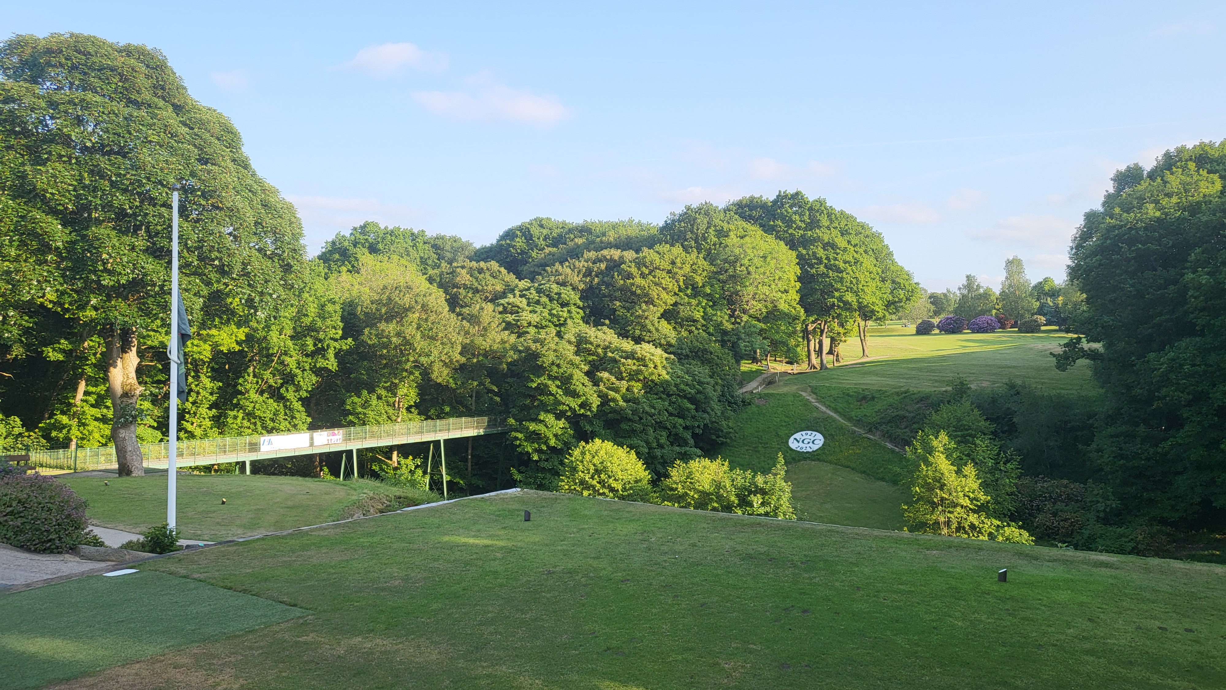 Iron bridge spanning wooded valley with golf course behind